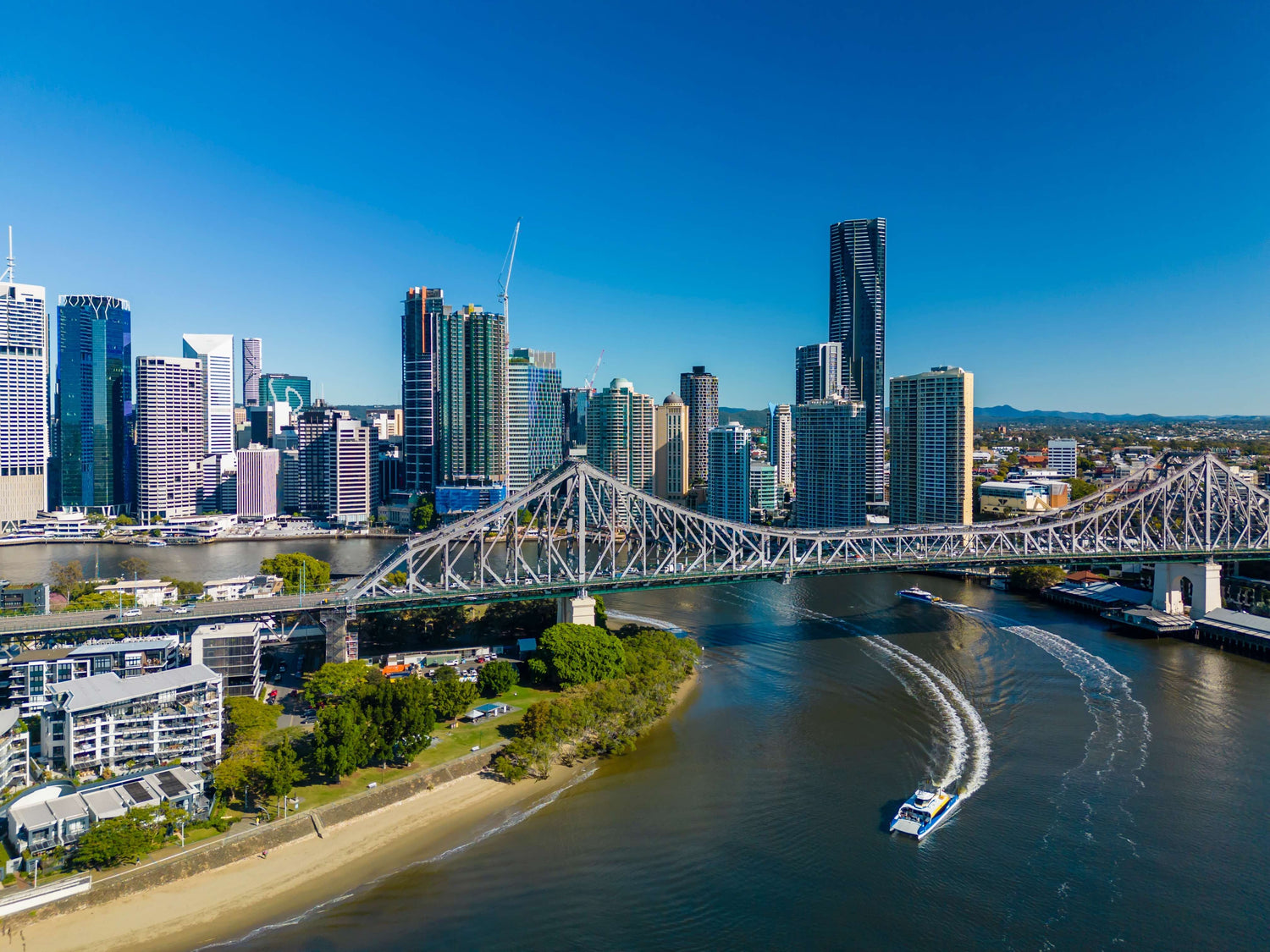 Brisbane skyline with the Storey Bridge over the Brisbane River, featuring modern buildings and boats.