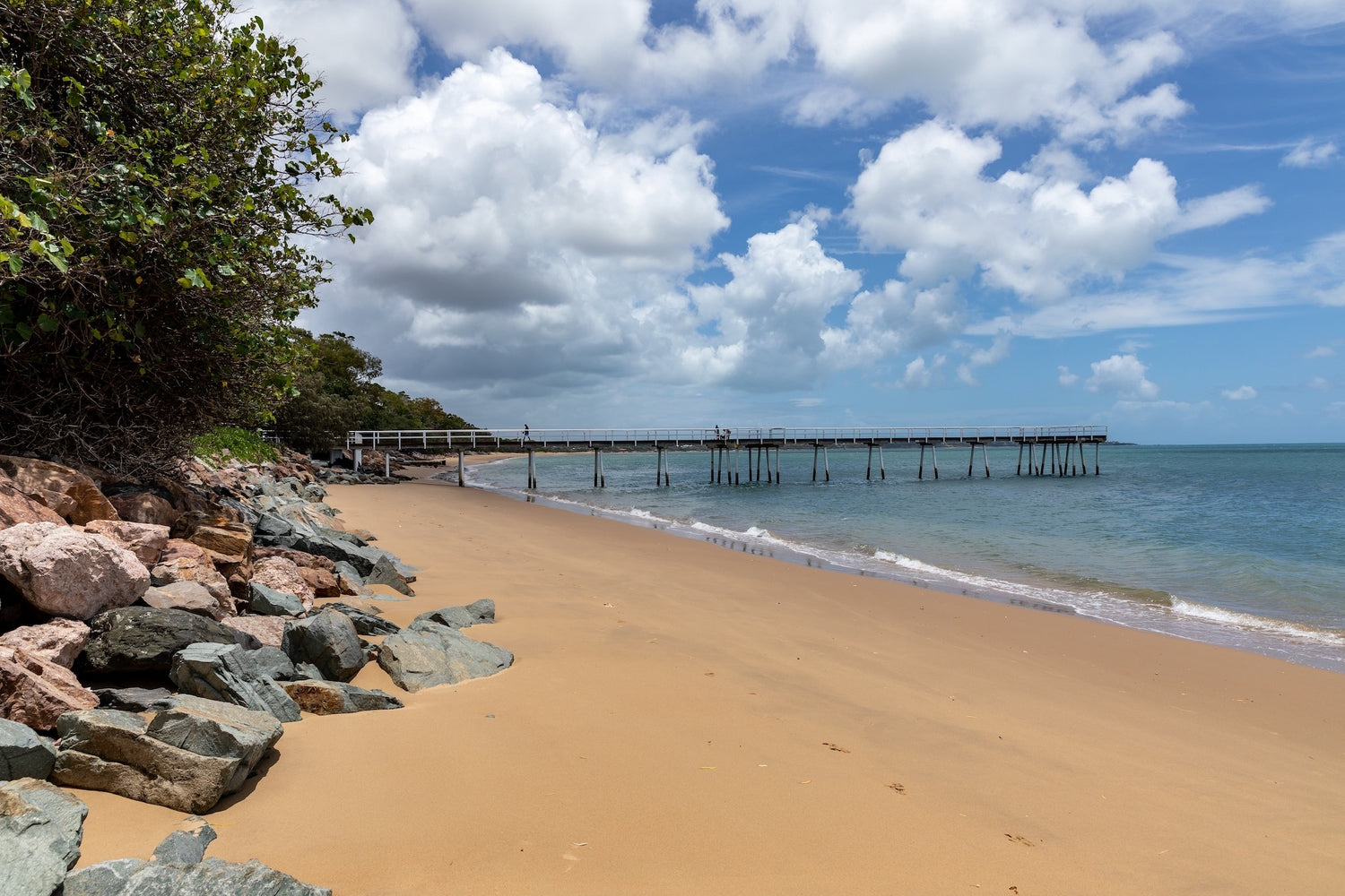 Hervey Bay beach scene with a pier extending into the ocean under a partly cloudy sky.