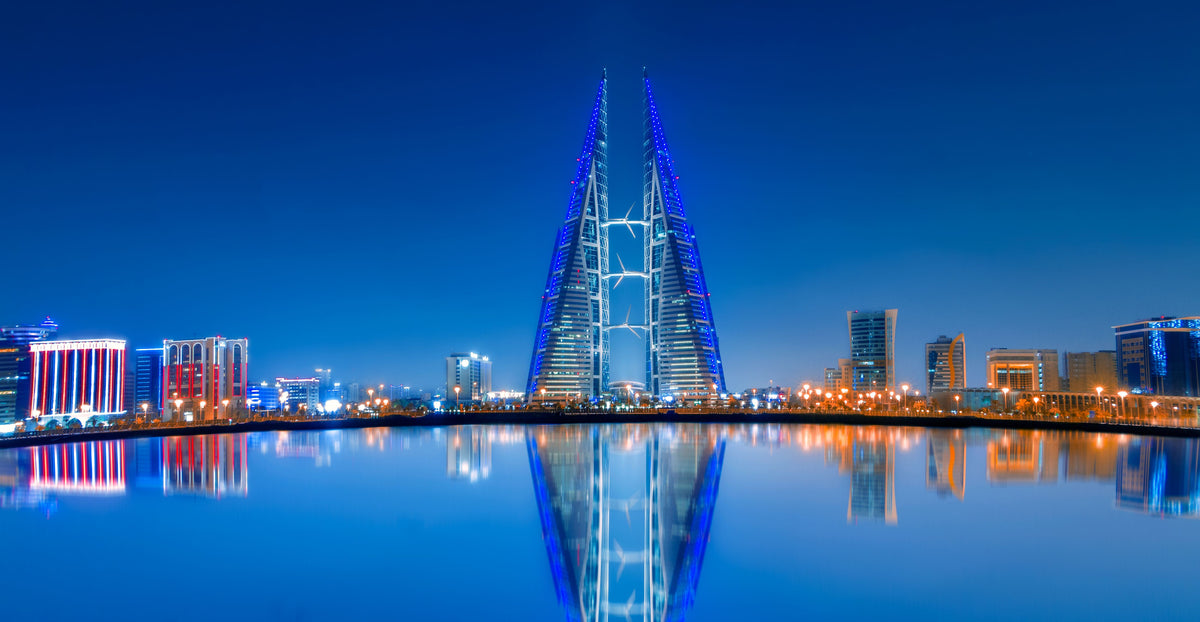 Picture of Bahain featuring blue water reflecting lit up buildings, skyscrapers and a blue sky.