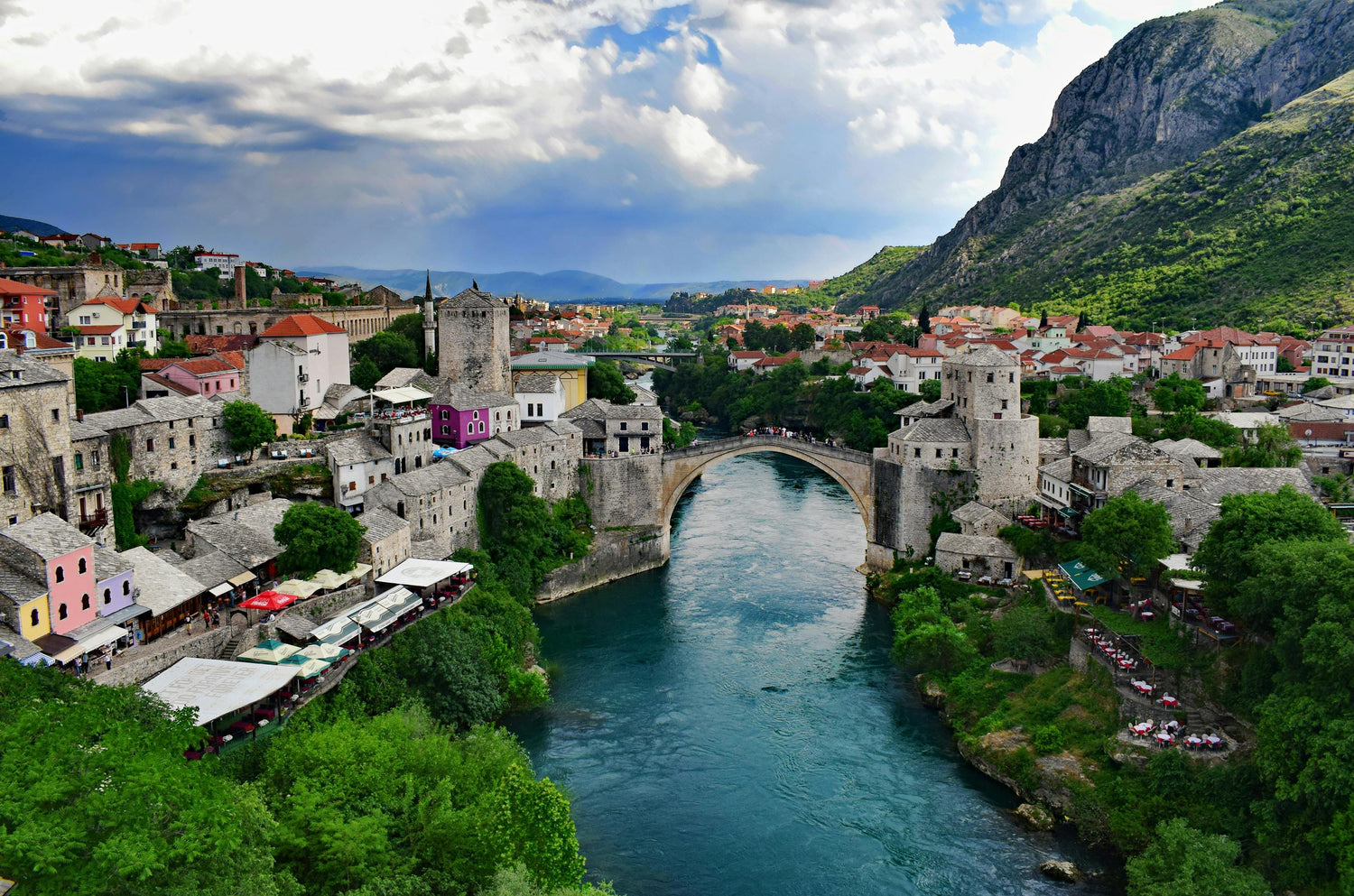 Village with historic bridge over a river, surrounded by mountains and greenery