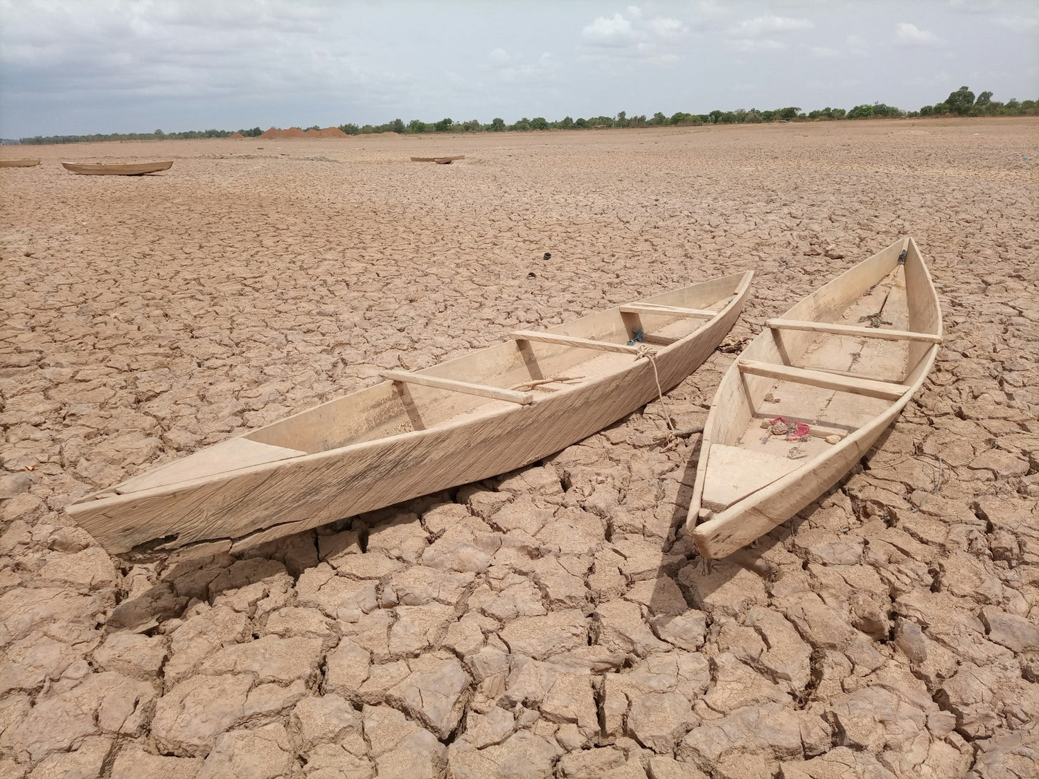 Two wooden boats on a cracked, dry lake bed with a clear sky.