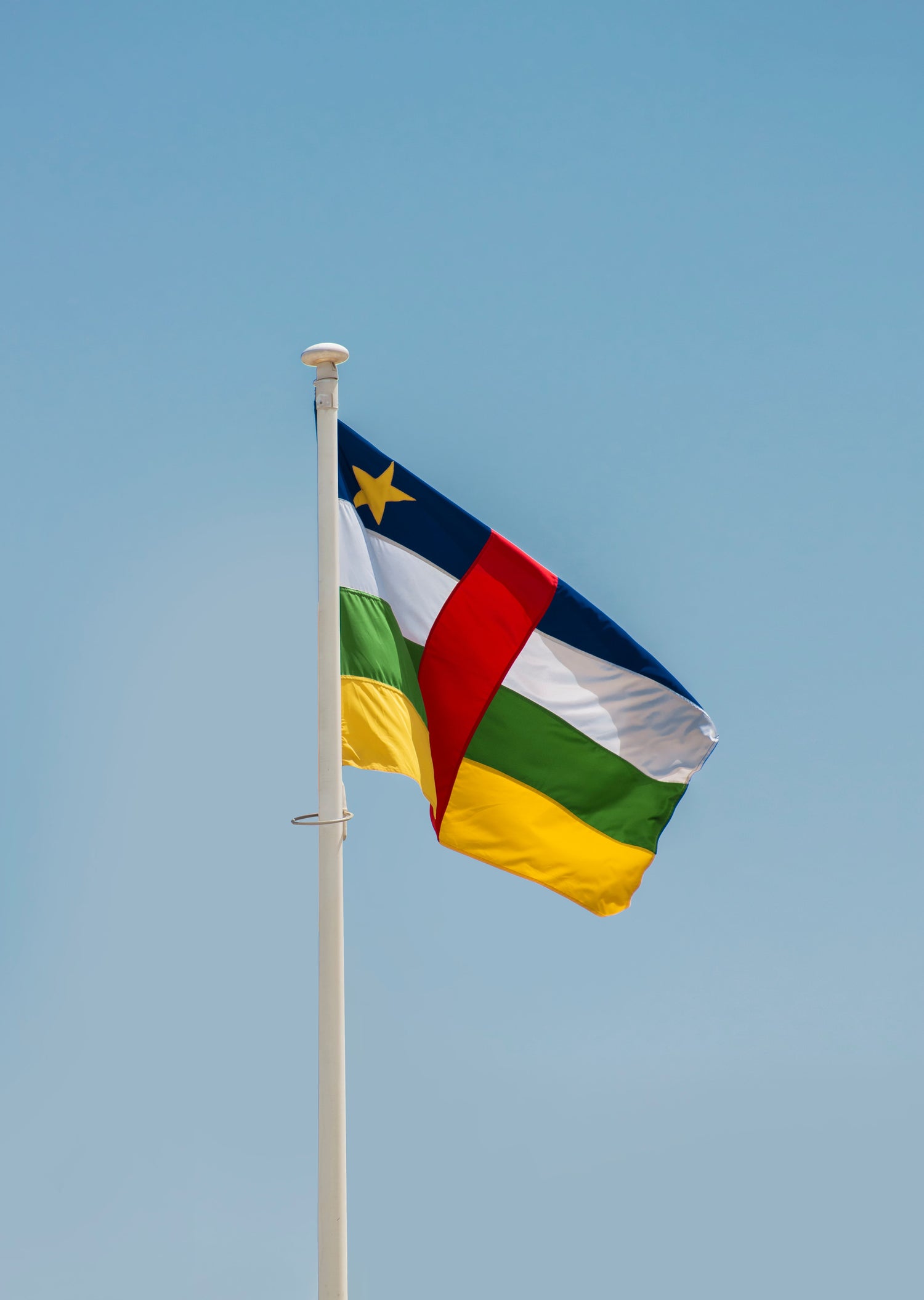 Picture of the flag of the Central African Republic with red, yellow, green, and blue colours on a clear blue sky background.