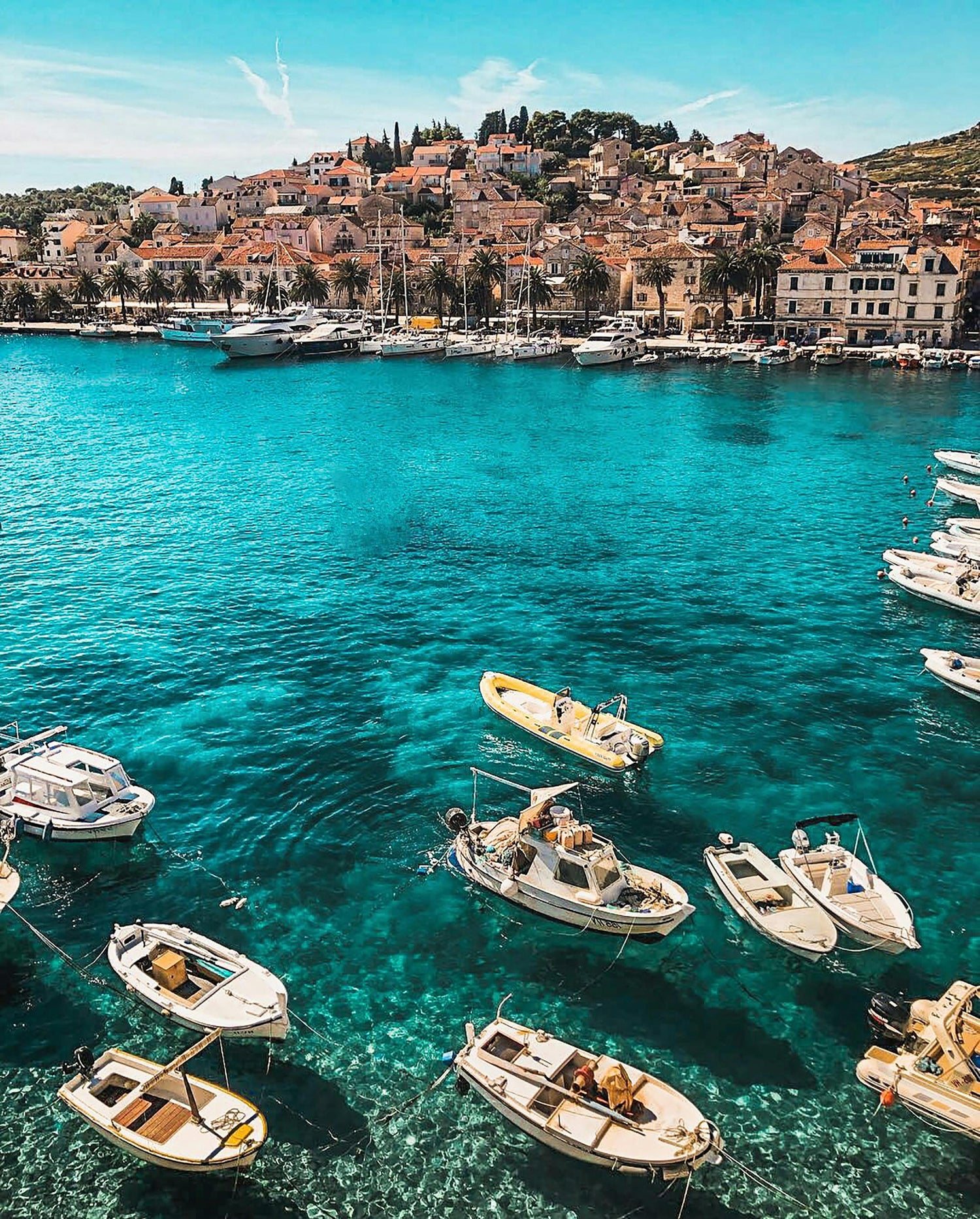 Harbour scene in Croatia with boats in clear blue water and a coastal town in the background