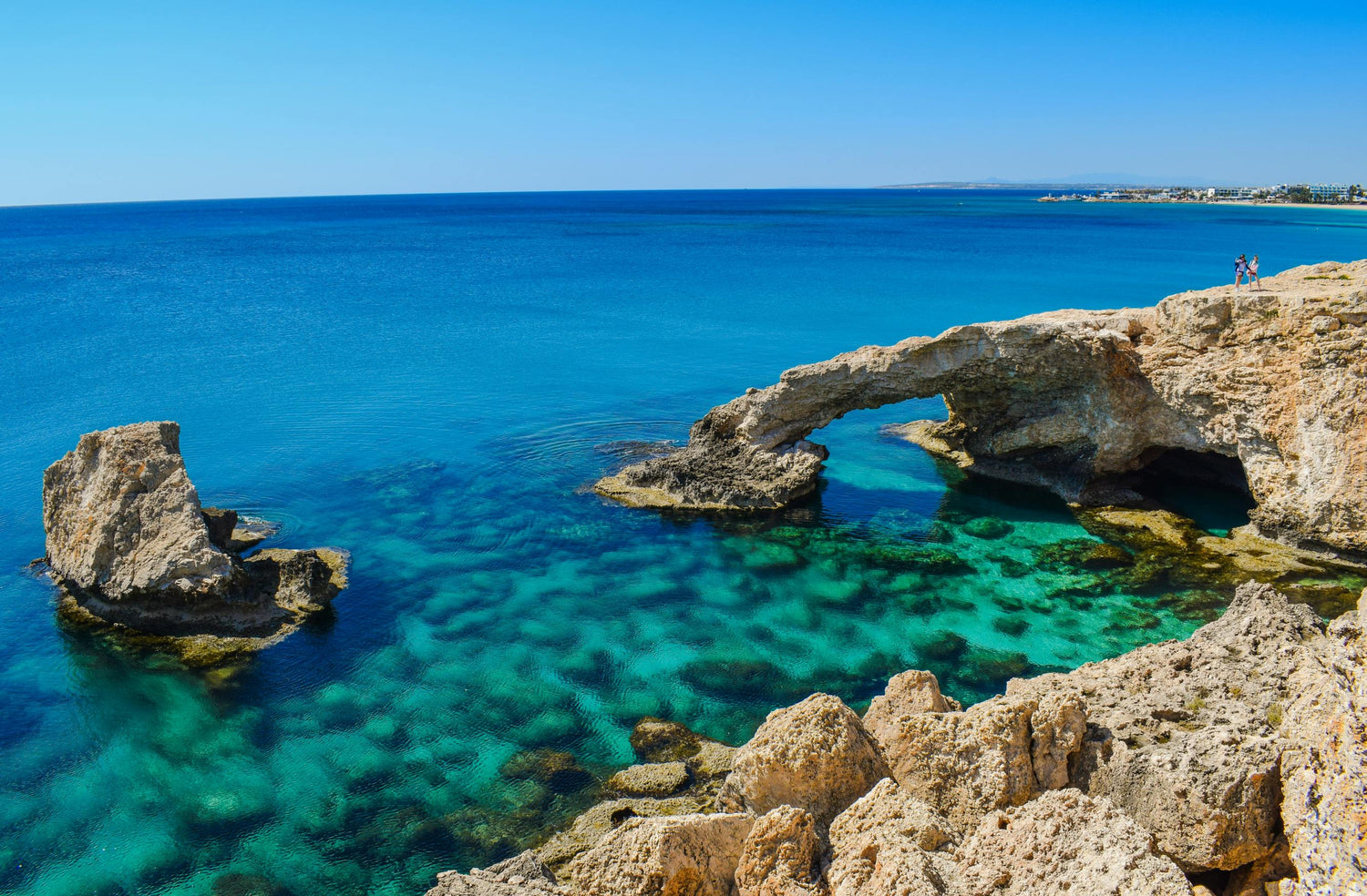 Rocky coastline in Cyprus with a natural arch over clear blue water on a sunny day.