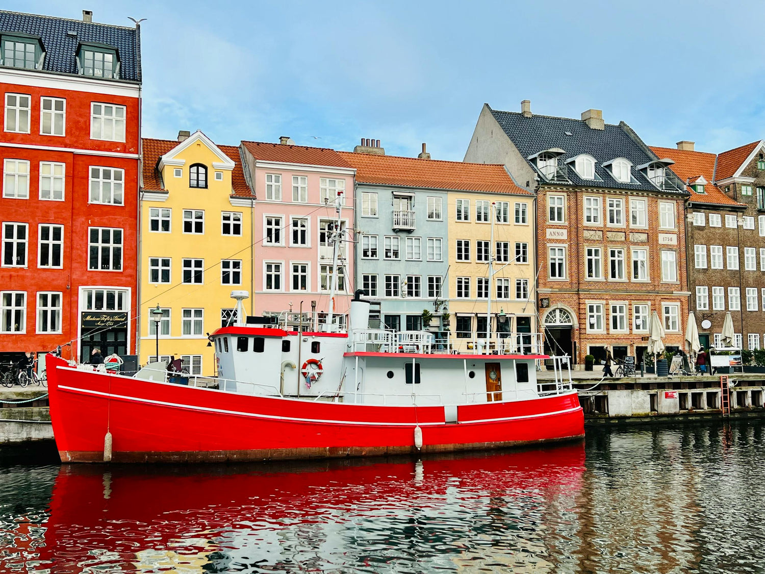 Red boat docked in a canal in Denmark with colourful buildings in the background