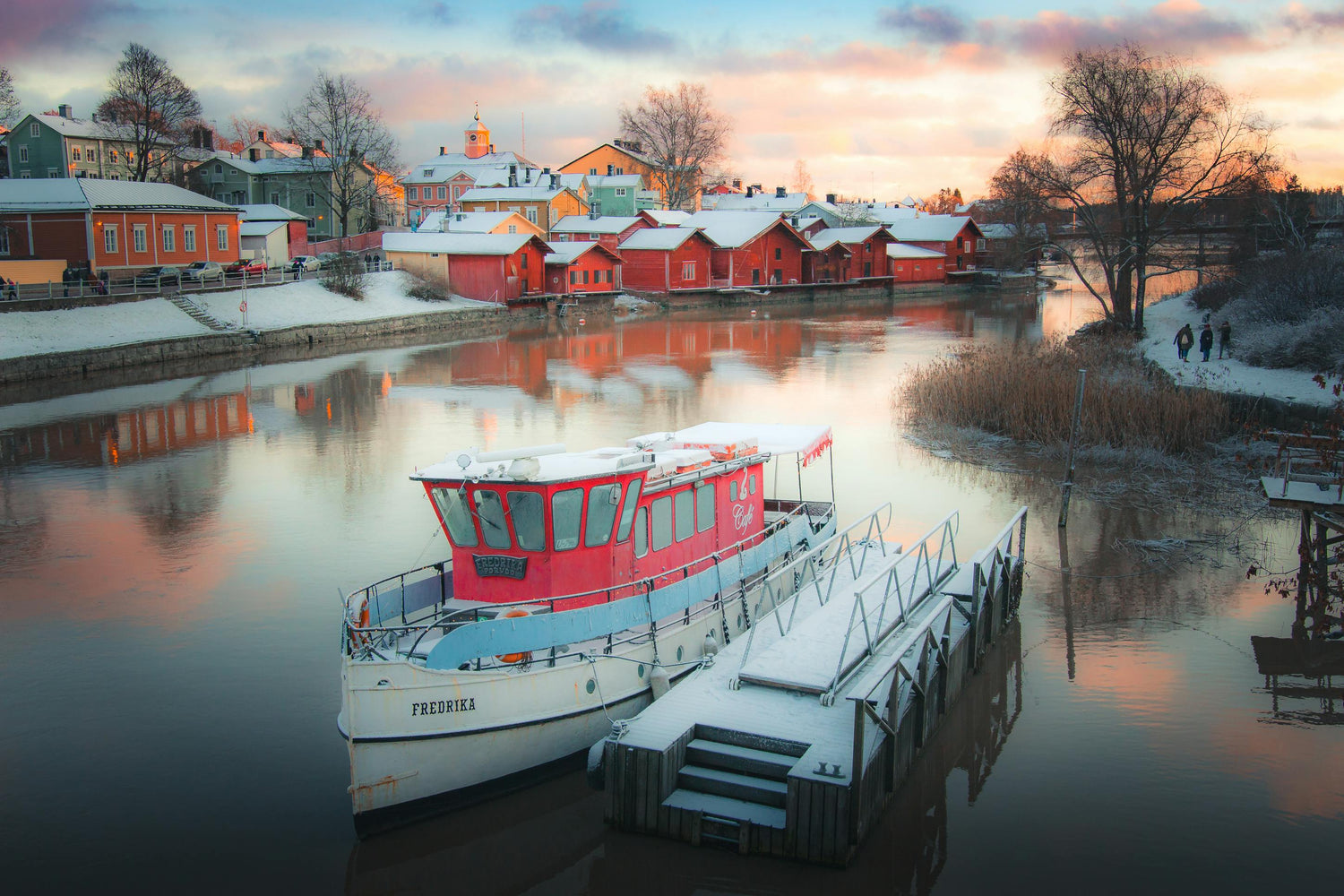 Red houses and a red boat at sunset in a snowy landscape in Finland.