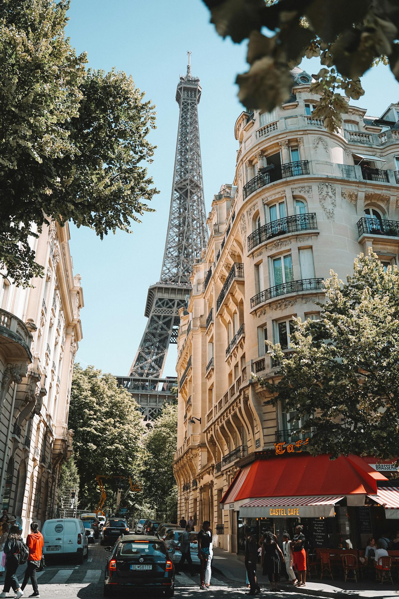 Street view of the Eiffel Tower in Paris with greenery and a cafe in the foreground.