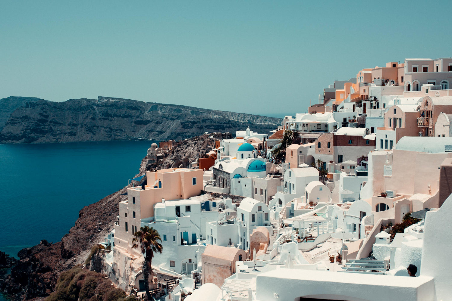 Greek village with white buildings and blue domes overlooking a body of water.