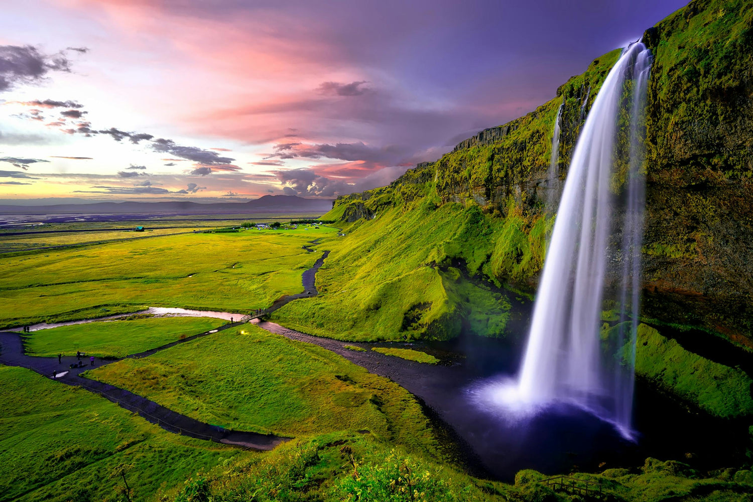 Waterfall cascading into a pool with a scenic landscape and colorful sky in Iceland.
