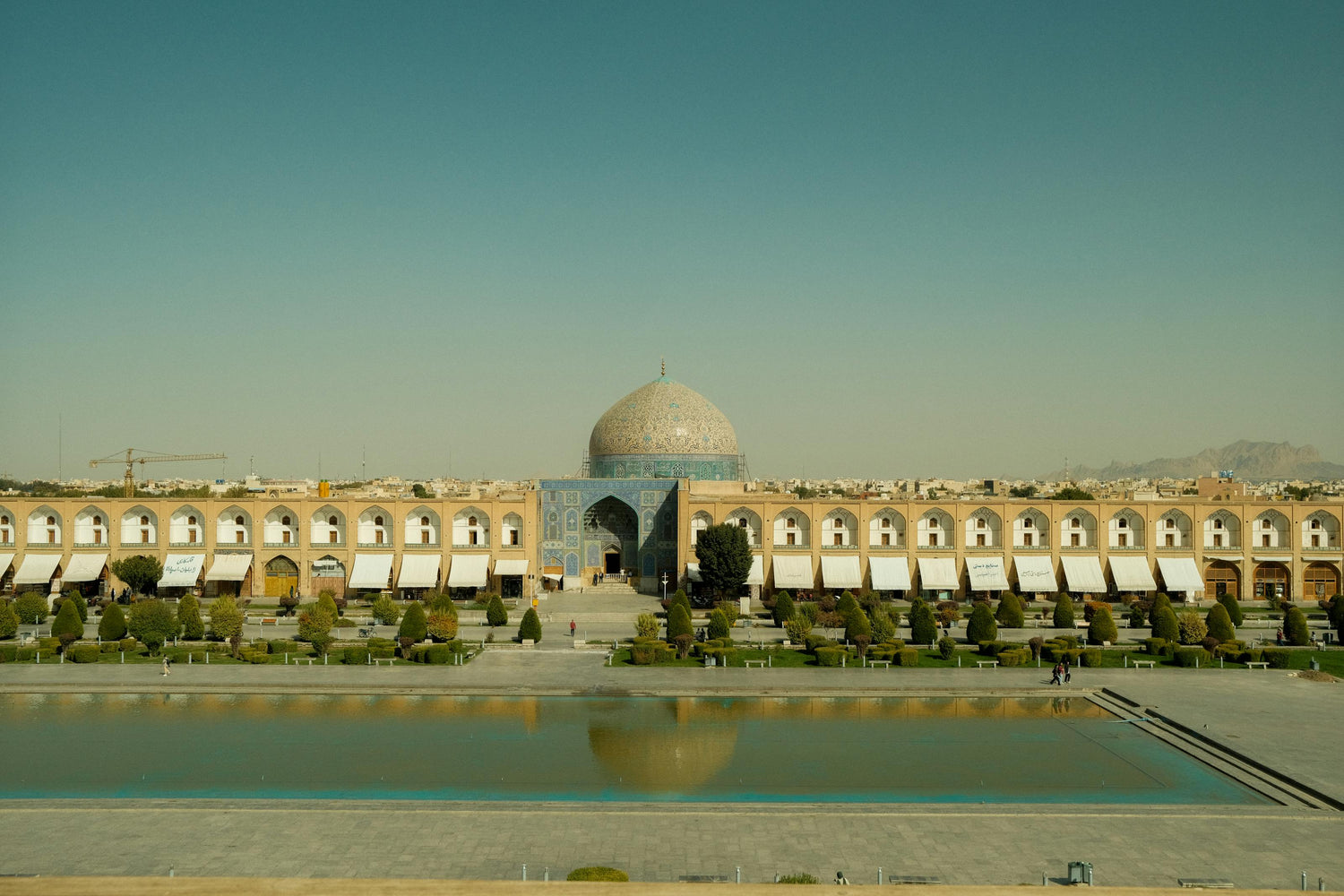 Historic building in Iran with a dome and reflecting pool in front, under a clear blue sky.