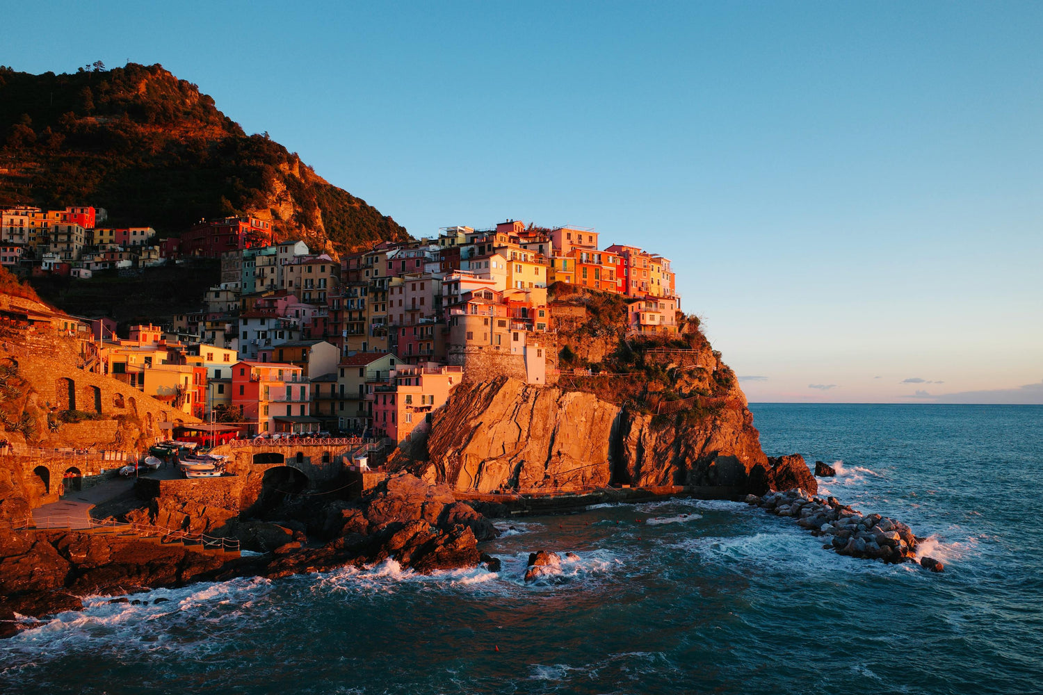 Hillside village in Italy with colourful buildings overlooking the ocean at sunset.