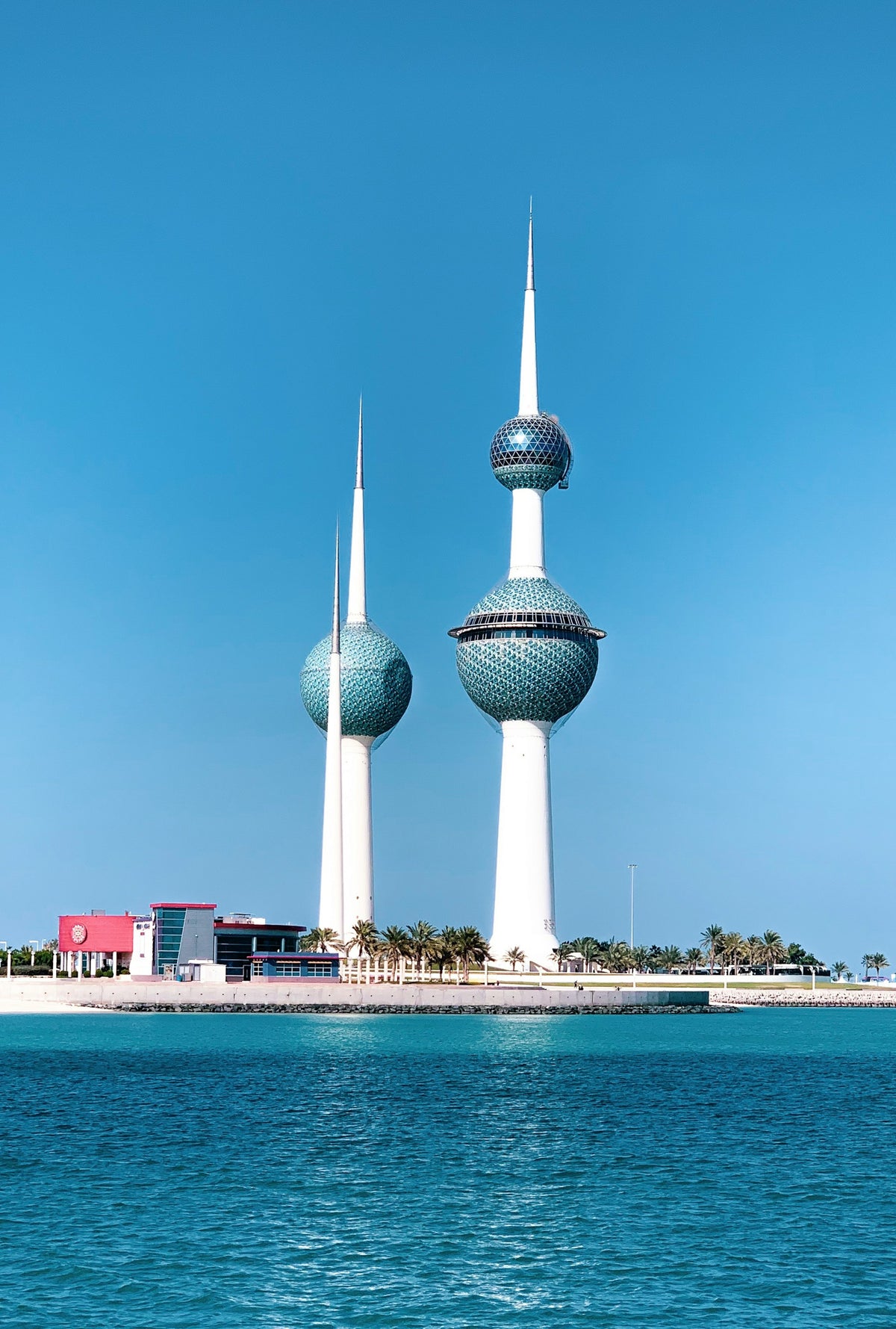 Two tall towers in Kuwait, with spheres in the middle, a blue sky in the background, and water in the foreground