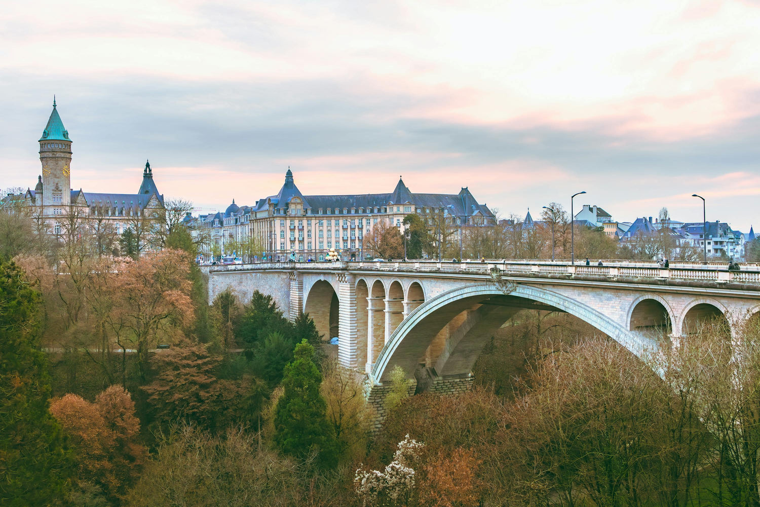 Picture of bridge leading to historic buildings with colourful autumn trees and a cloudy sky