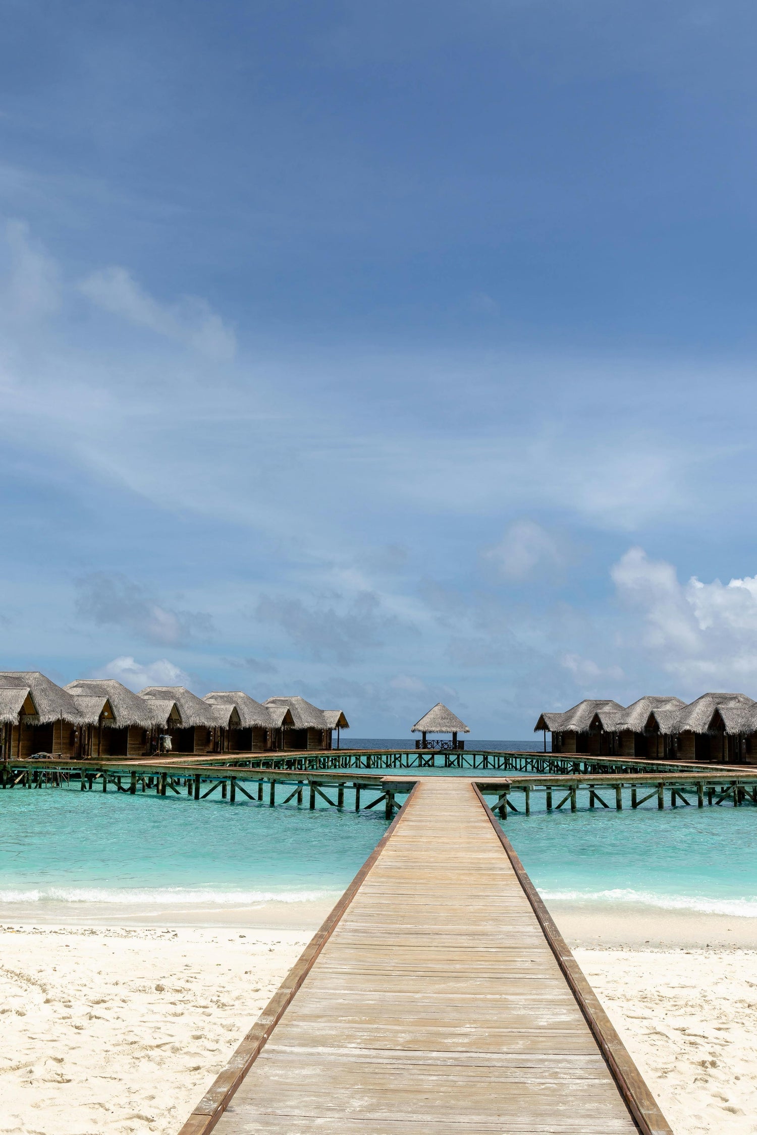 Beach in the Maldives with a wooden walkway leading to thatched-roof huts over water