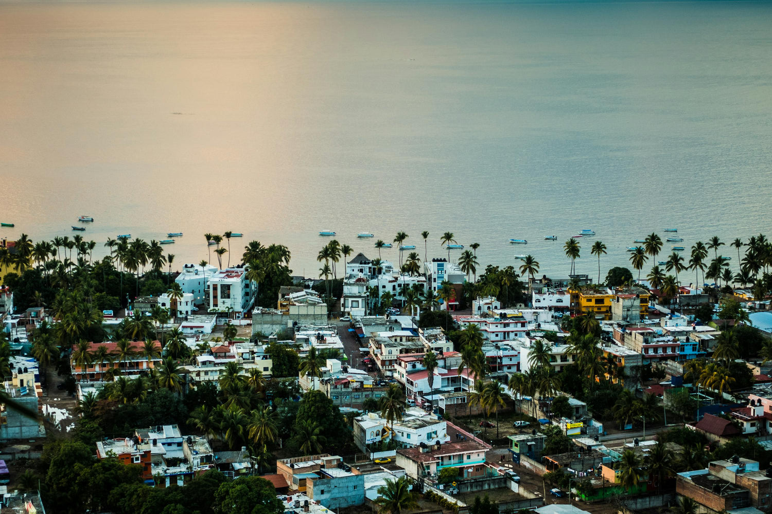 Aerial view of a coastal town in Mexico with buildings and palm trees under a sunset sky.