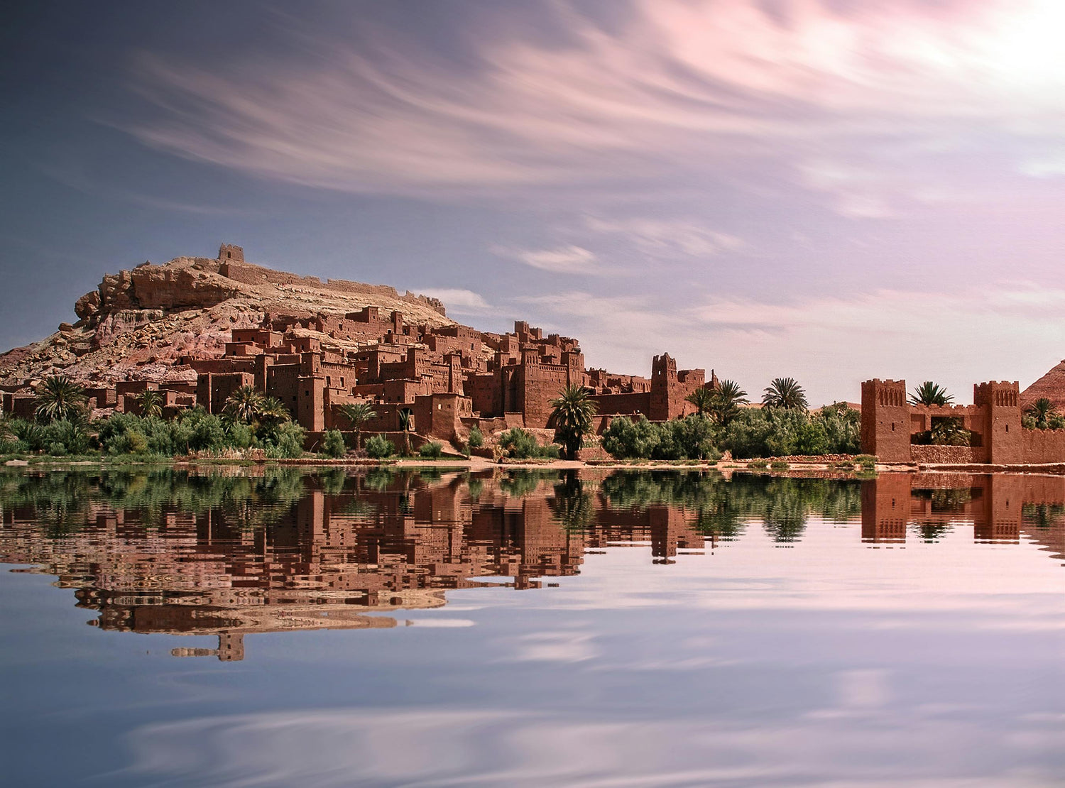 Traditional Moroccan kasbah reflected in a calm lake with a mountainous background