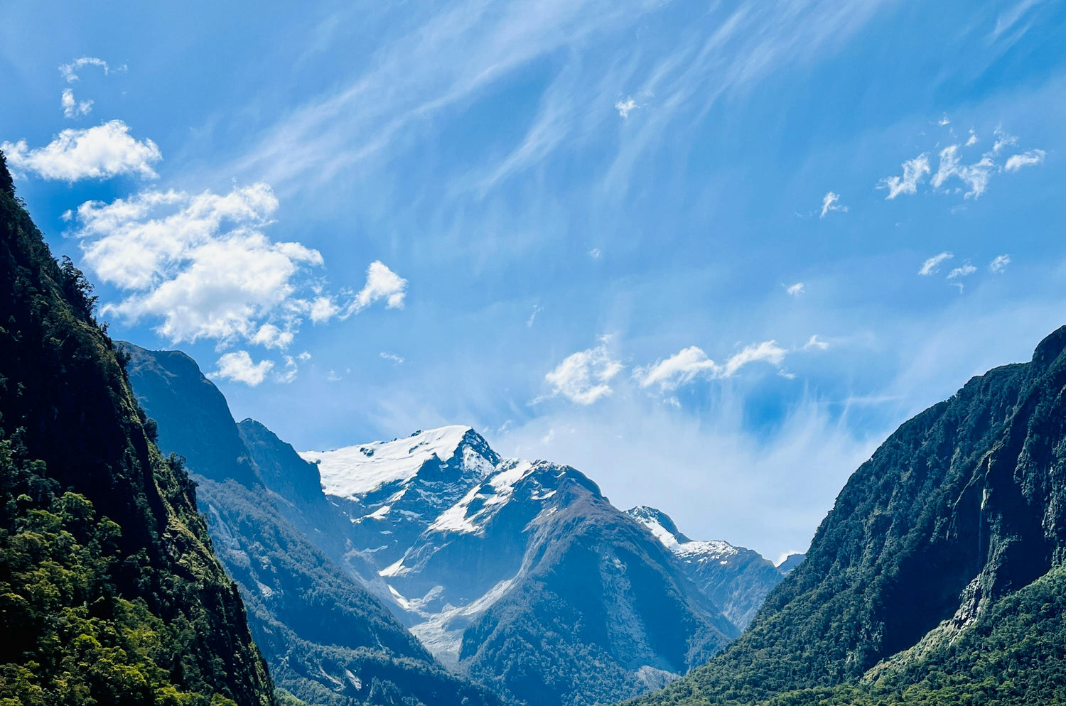 Mountain range of Milford Sound with snow-capped peak under a blue sky with scattered clouds