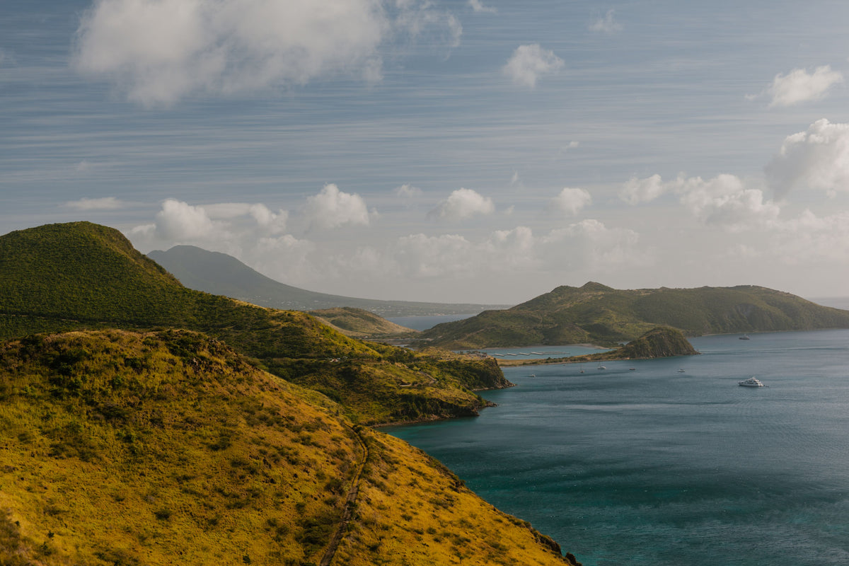 Picture of Saint Kitts and Nevis, featuring rugged mountainous coastline terrain with blue water and a blue cloudy sky