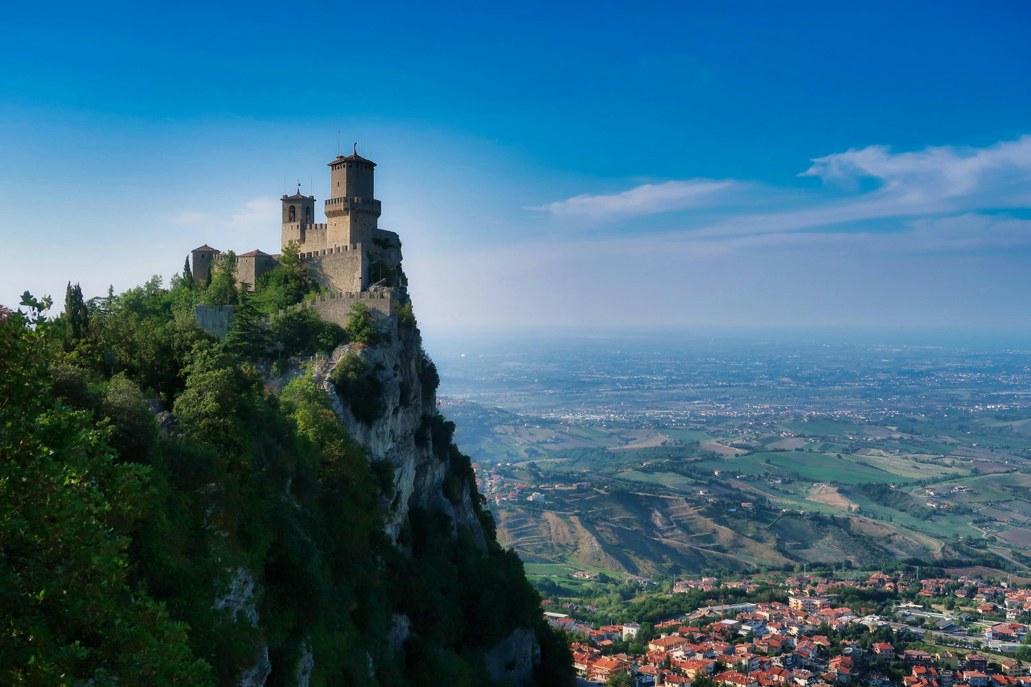 San Marino featuring a castle on a cliff overlooking a valley with a town below