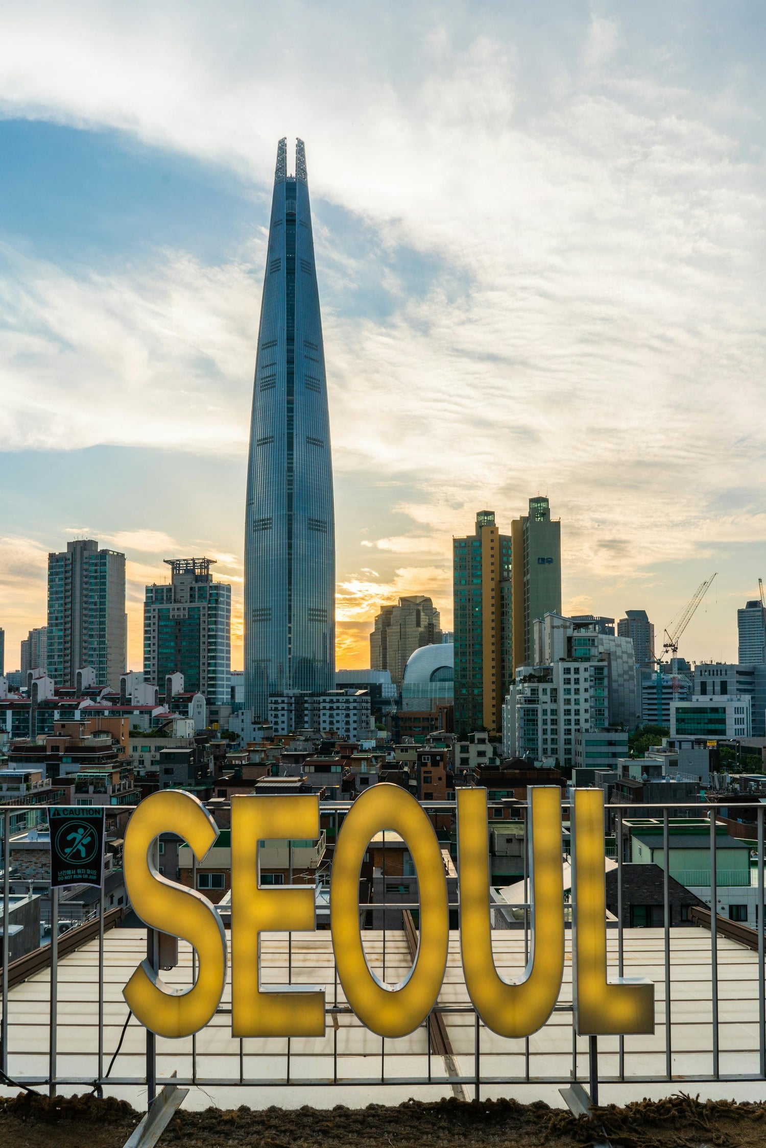 Cityscape with a tall building and 'SEOUL' sign against a cloudy sky.