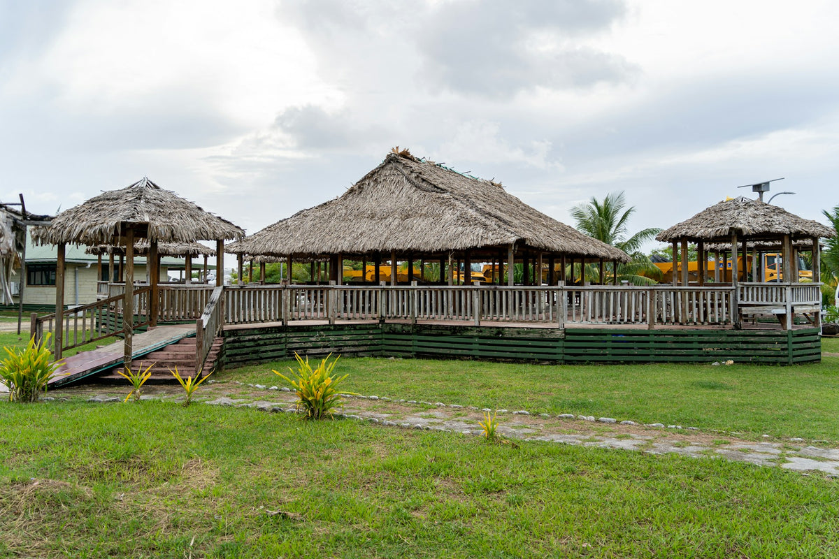 Three thatched-roof wooden pavilions or cabanas with elevated platforms and railings, situated on a grassy lawn under an overcast sky in Tuvalu.