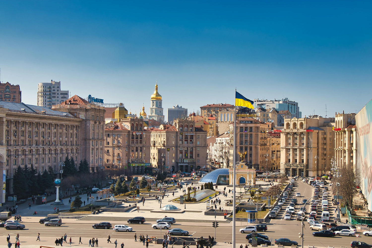 Cityscape in Ukraine with a large flag and architectural buildings under a clear blue sky.