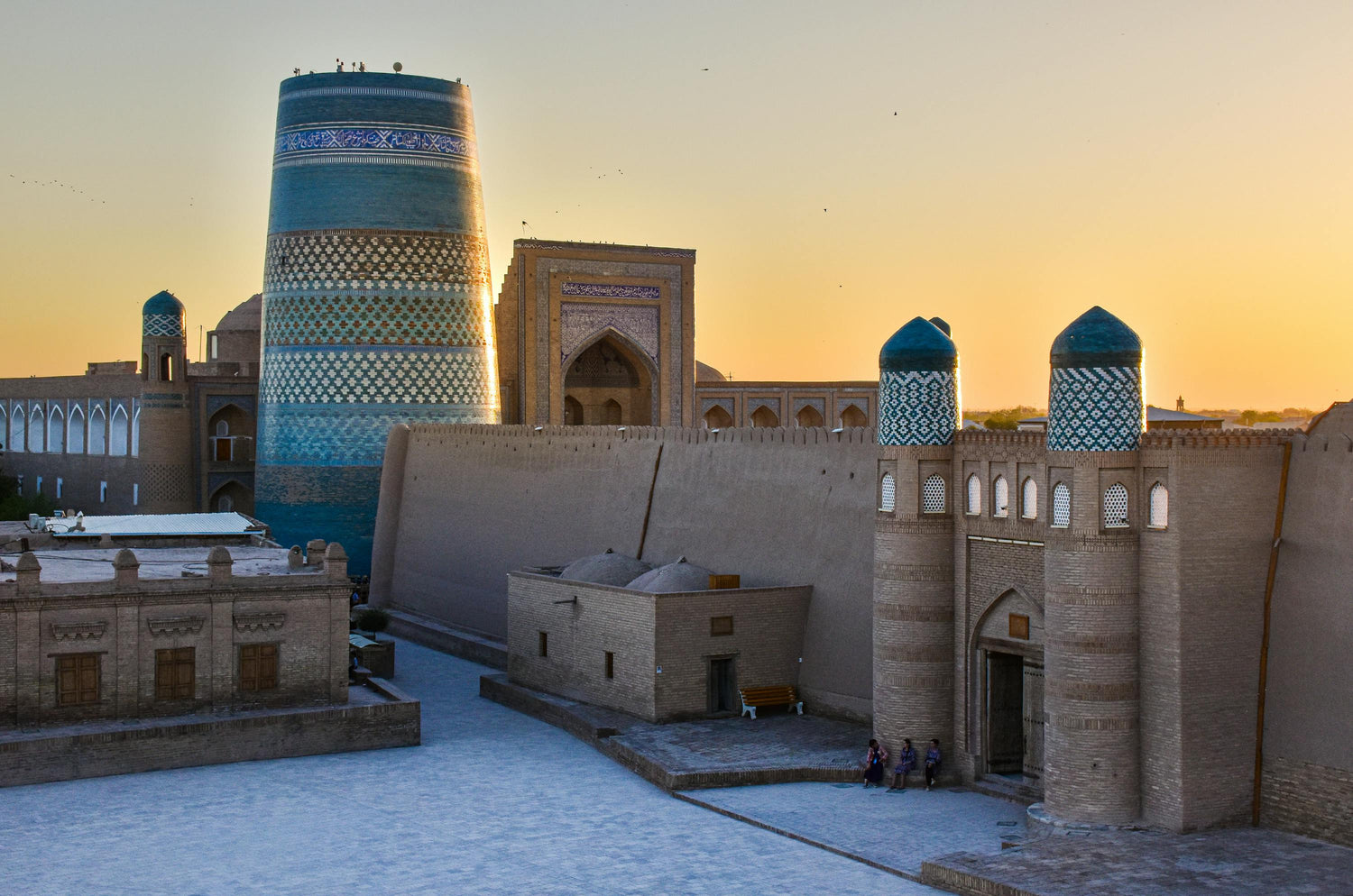 Historic architectural complex in Uzbekistan with a prominent blue tower at sunset.