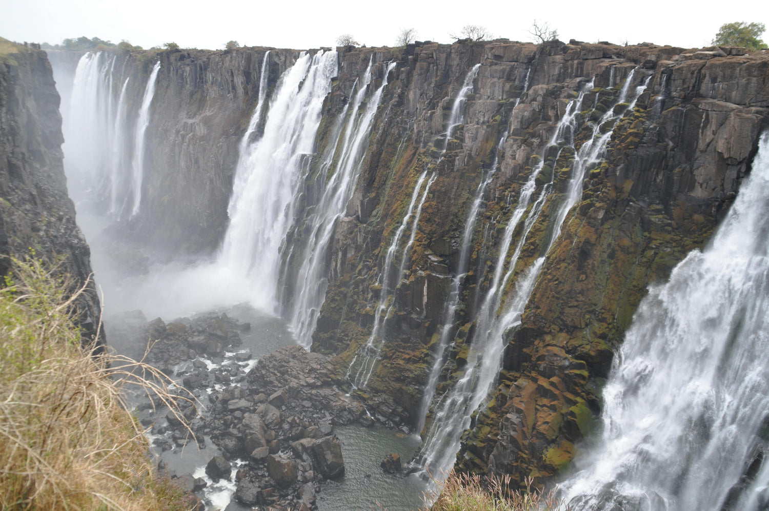 Victoria Falls cascading down a rocky cliff with surrounding vegetation.